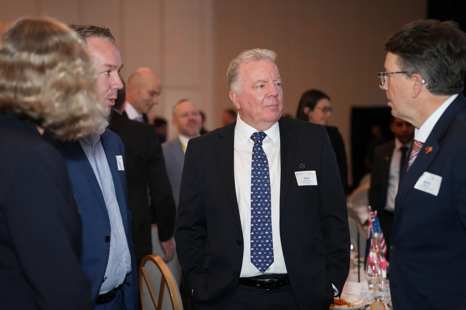 Delegates networking in business attire at an AmCham conference in Brisbane, with name badges and table flags.